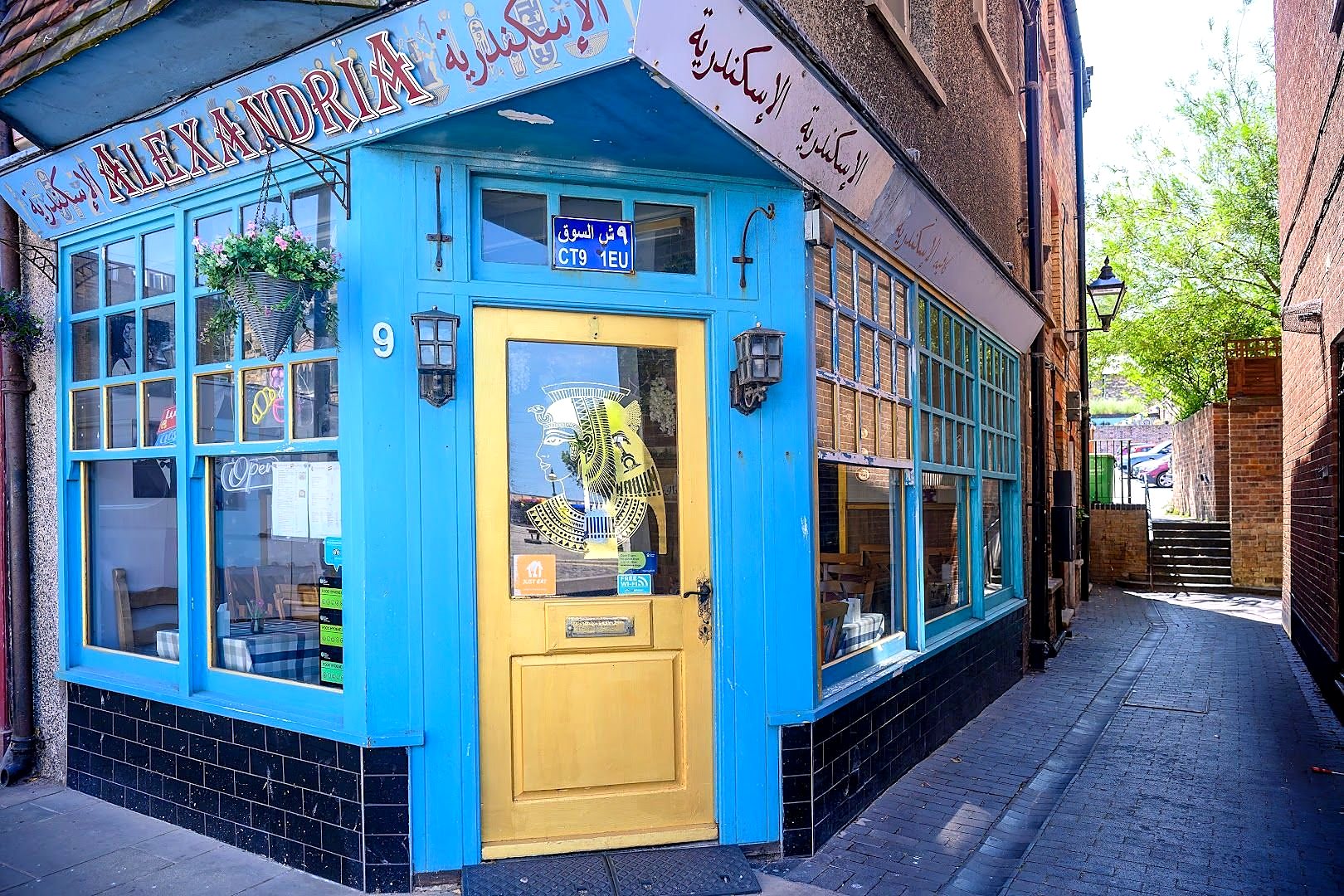 Alexandria Café on the corner of Market Street, Margate: a sky-blue shopfront with a yellow door, the name in English and Arabic above the windows, and plants hanging by the door